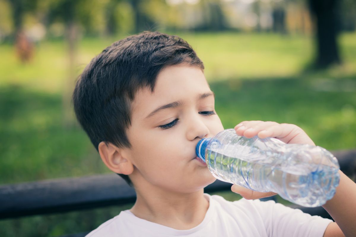 A kid rehydrating himself with water from a plastic bottle