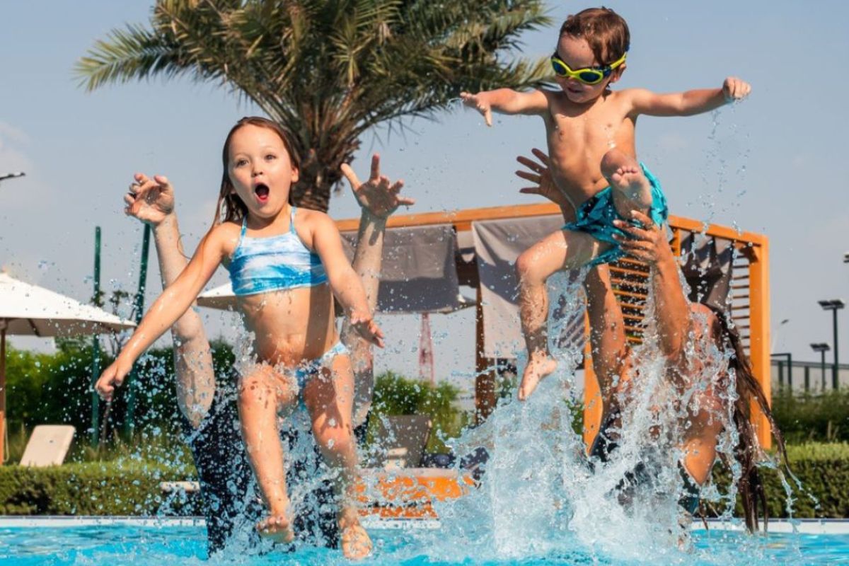 2 kids enjoying at the pool while being splashed and thrown off air by adults at Yas Acres Golf & Country Club summer offers 2024