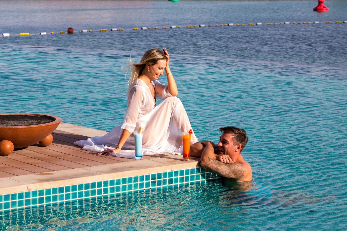 A lady by the poolside and a guy inside the pool with drinks at Grand Hyatt Abu Dhabi summer offers