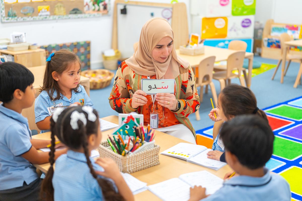 5 kids paying attention to the teacher who is discussing inside the classroom and at the back there's wooden table and chairs at Cranleigh Abu Dhabi school pre-prep