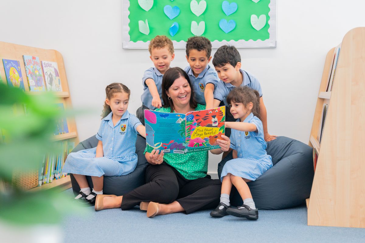 Teacher and kids sitting, 5 kids pointing in the book while teacher is holding the book at Cranleigh Abu Dhabi school