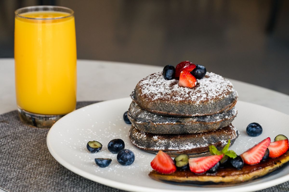 Orange juice and a yummy plate of chocolate pancake sprinkled with powdered sugar and garnished with berries at Roots Bar & Kitchen Yas Acres Golf & Country club breakfast in Abu Dhabi