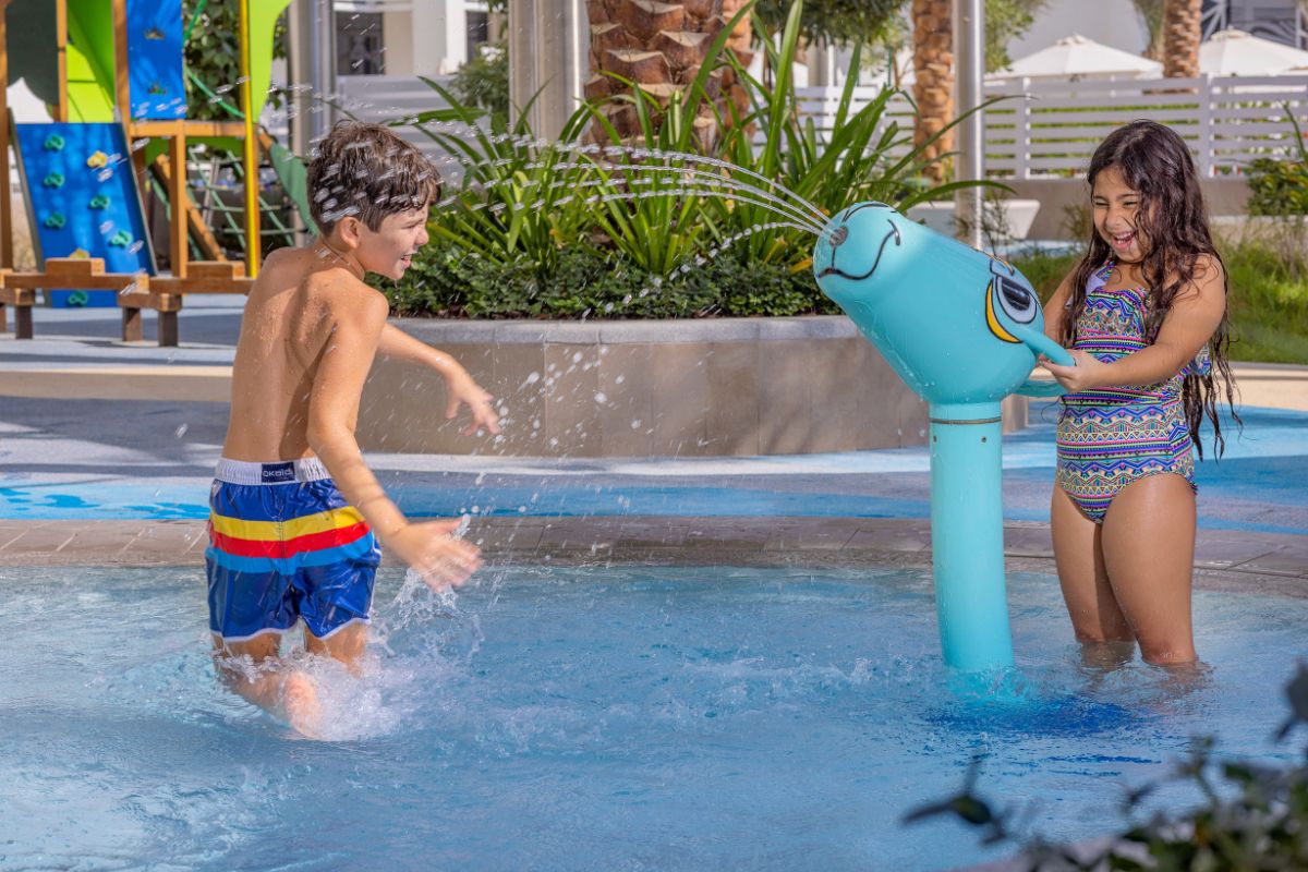 2 kids playing on the pool with a spraying toy at Hilton Yas Island for kids summer camp