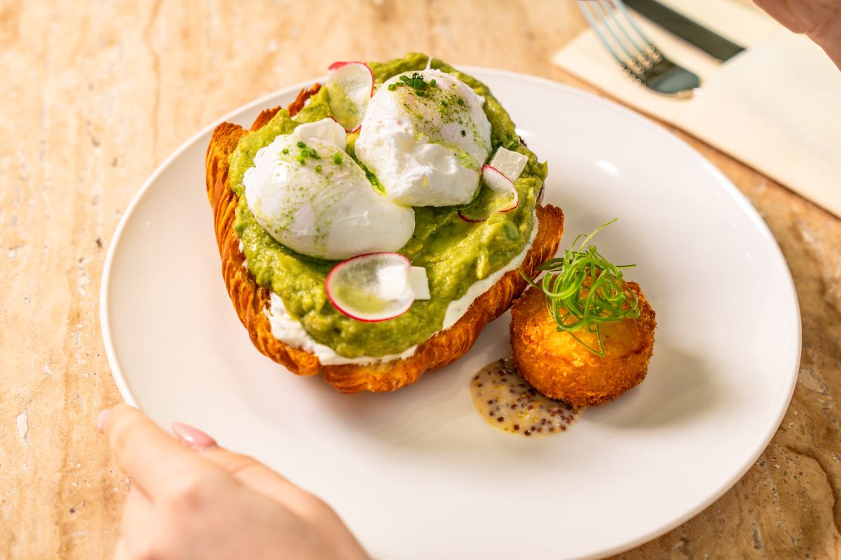 James at Al Qana featuring a croissant topped with smashed avocado, poached egg drizzled with sauce and garnished with radish plus a croquette on the side with a dijon mustard sauce