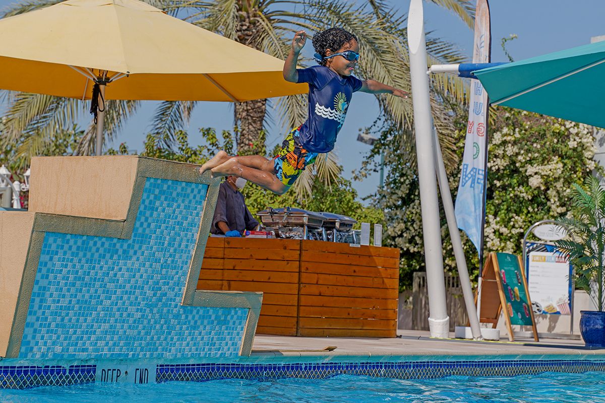 A kid jumping off the pool at The Club Abu Dhabi summer camp