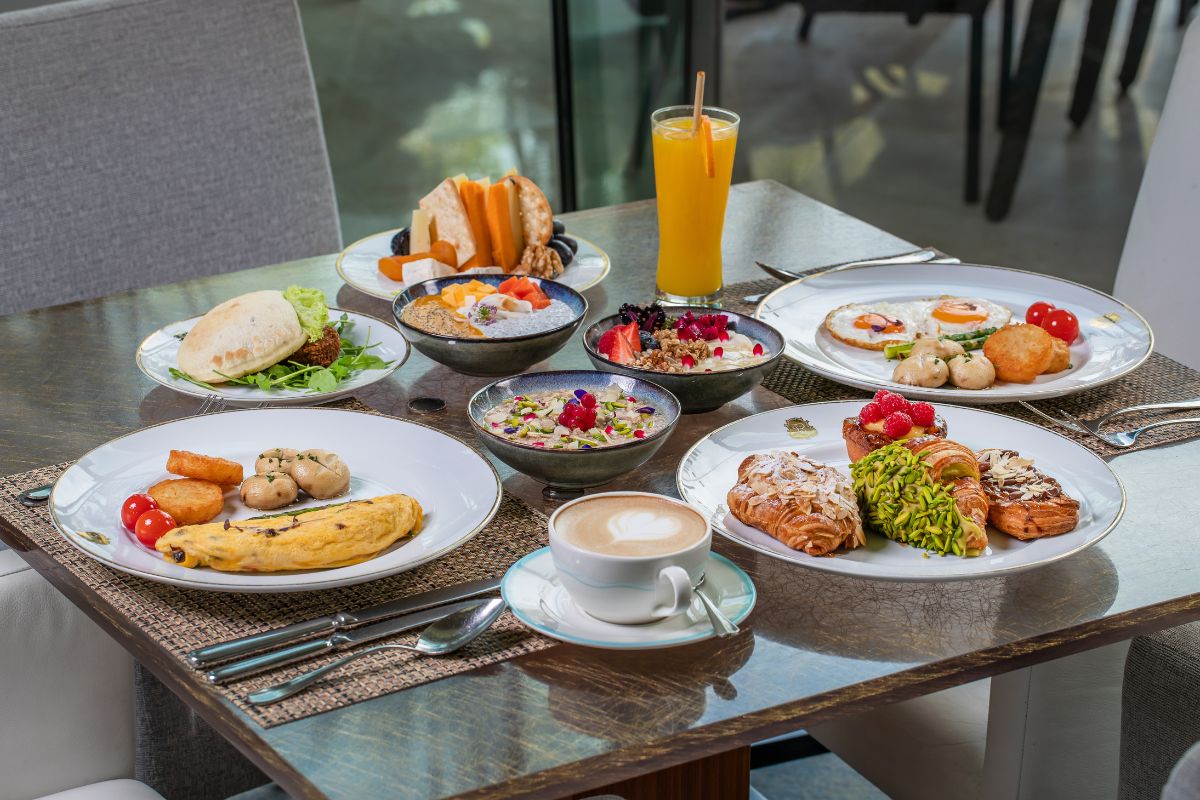 The St. Regis Saadiyat Island Resort Abu Dhabi with a table full of breakfast dishes including bread, granola and breakfast bowls, omelette plates, croissants, eggs, orange juice and coffee