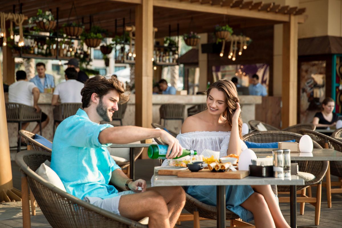 Nasma Beachfront at Saadiyat Rotana Resorts and Villas outdoor seating, a couple enjoying meals and the guy pouring sparkling water onto glasses