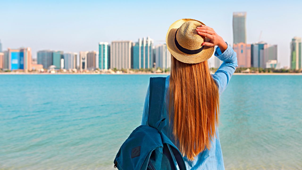 Woman with backpack weaing the hat. On the background is panorama of Abu Dhabi
