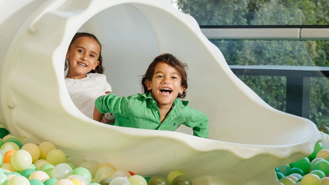 two children going down a slide at Little Acres Kids Club, Yas Acres Golf & Country Club