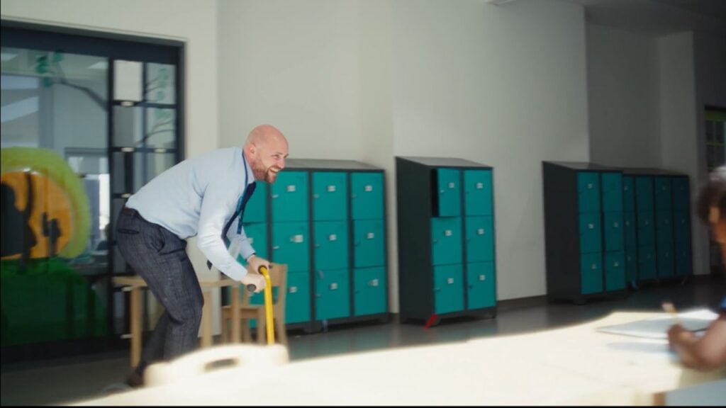 Man riding a scooter indoors with lockers in the background.