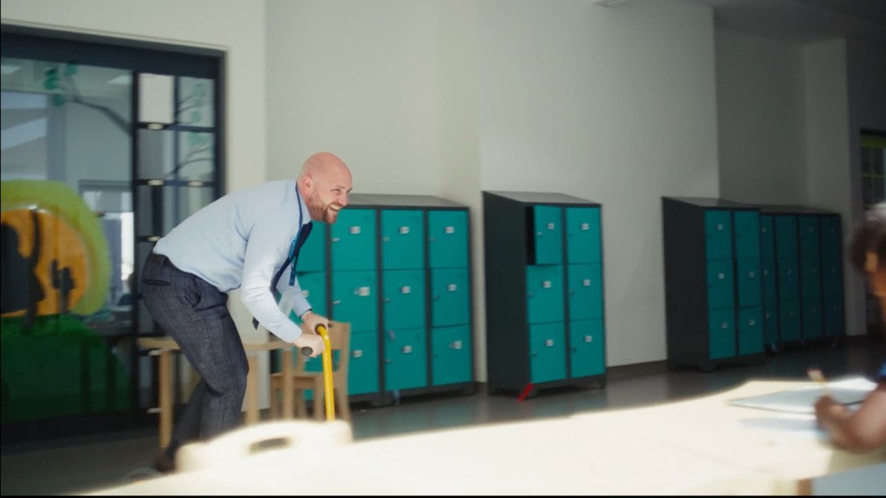 Man riding a scooter indoors with lockers in the background.