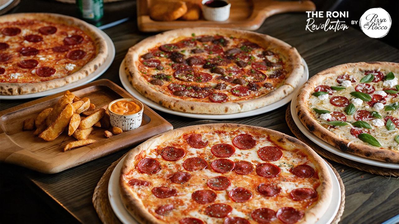 Table full of pizza with a logo of Pizza Di Rocco on the top right corner