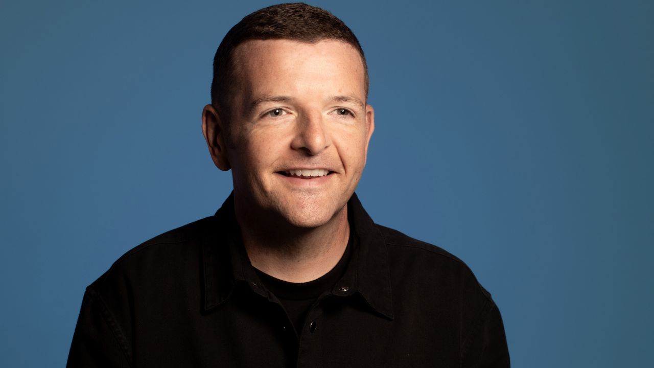kevin bridges smiling with blue backdrop