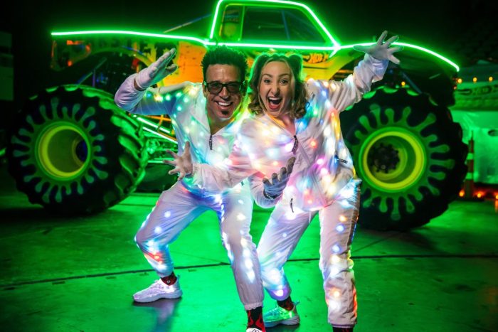 A couple excitingly posing in front of a glow in the dark Hot Wheels Monster Truck for Live Glow in Etihad Arena Abu Dhabi