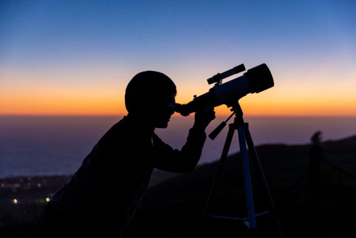 A silhouette of a person holding up a telescope during stargazing